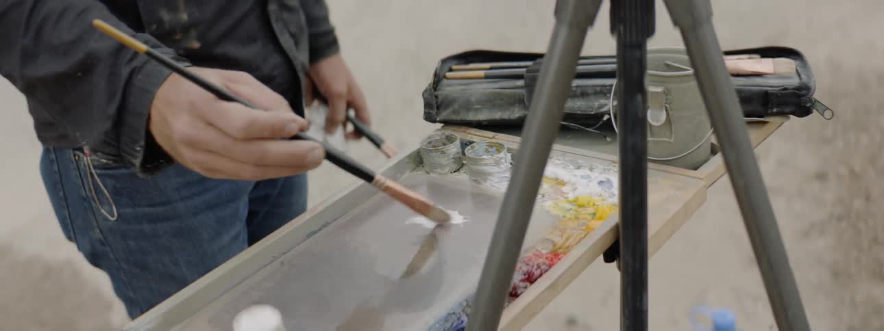 An artist painting on an easel near a roadway