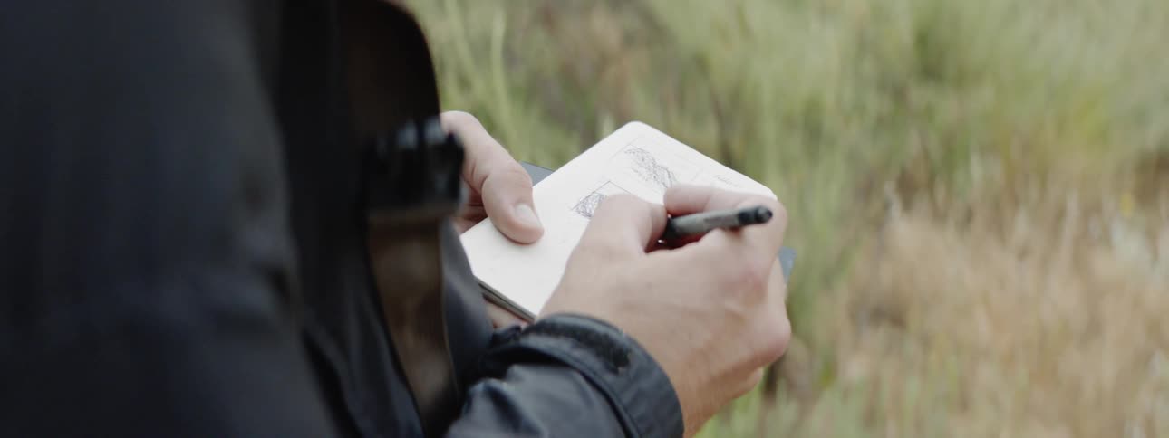 Hands of person sketching scenery in small sketchbook