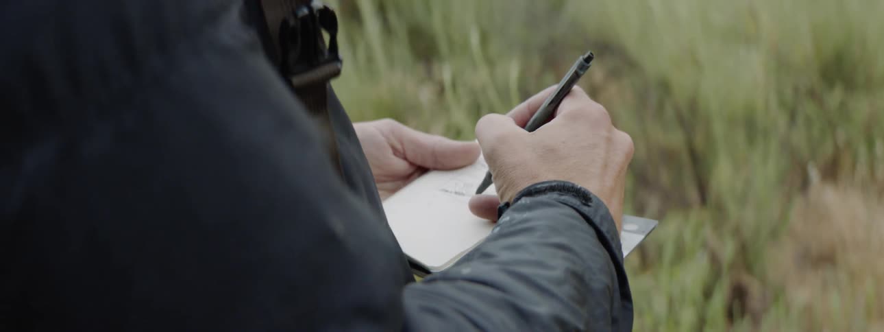 A person uses a pen to write on a small note pad