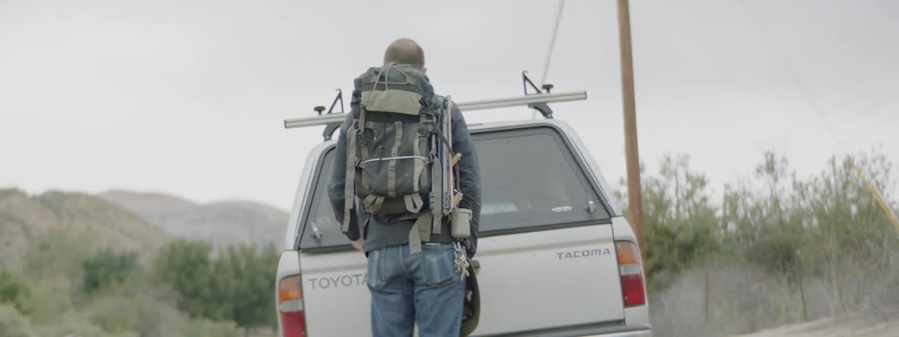 A man with a backpack closes up the back of his vehicle