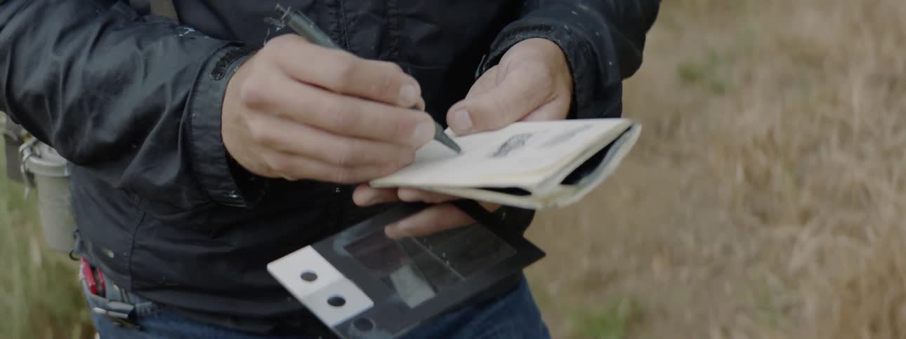 A person writing in a notebook out in a field