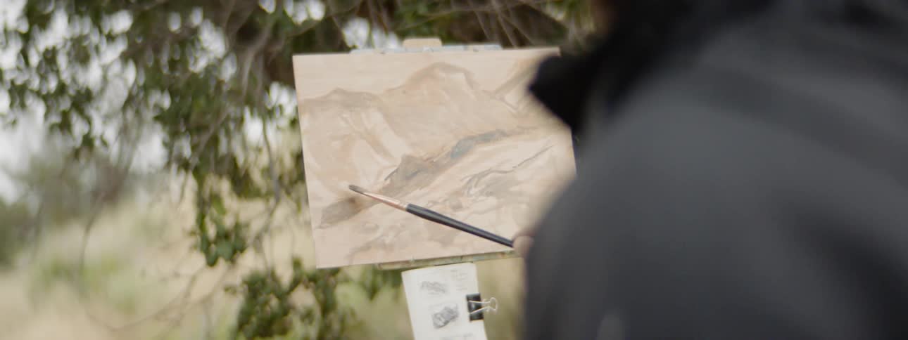 Man paints mountains on frame with brush in the nature by day