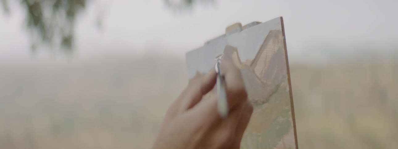 An artist paints on a small canvas outside in the fog