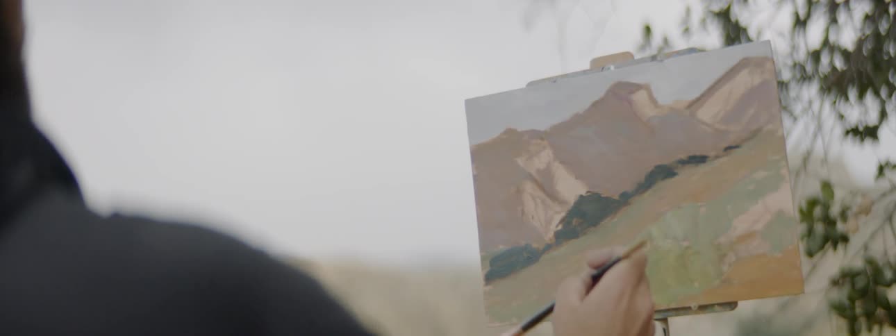 Man painting landscape with brush on canvas on easel outdoors