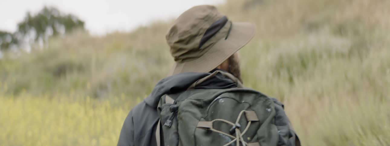 Man wearing backpack and hat walks in grassland in the daytime