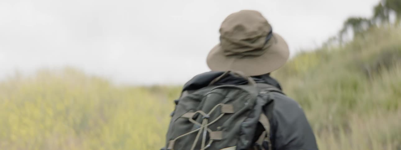 A man in a backpack walking up a grassy hill
