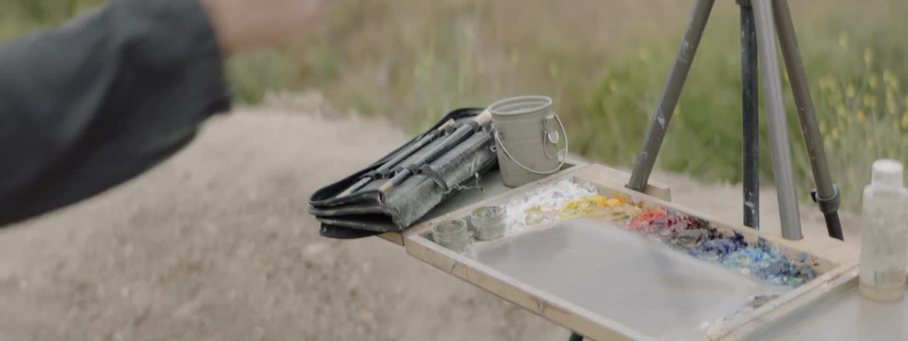 A painter rests his brushes on his canvas as his palette sits below