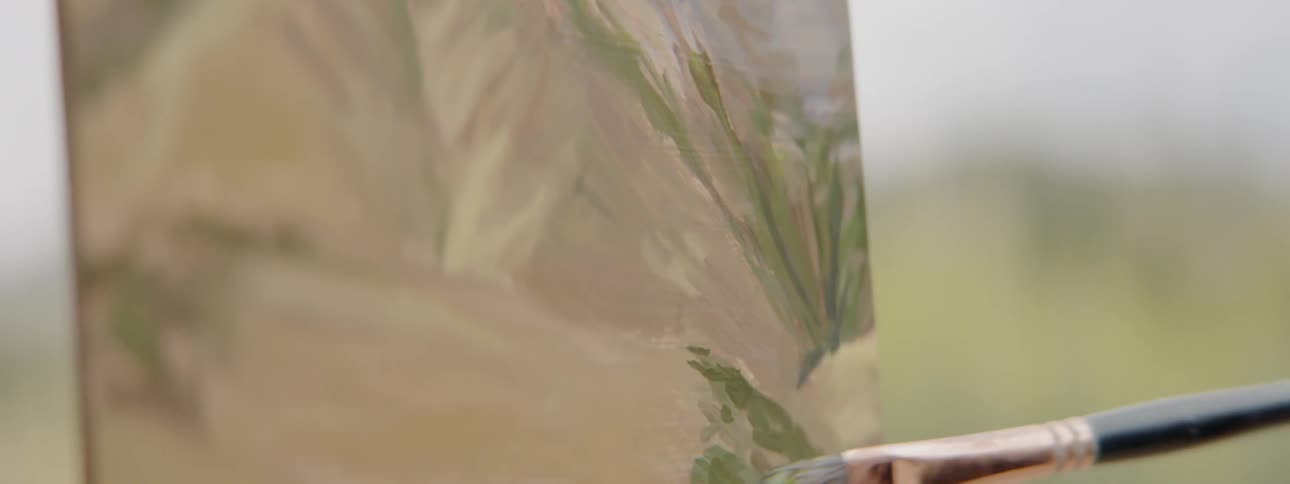 Green paint is brushed onto a canvas outside in a field