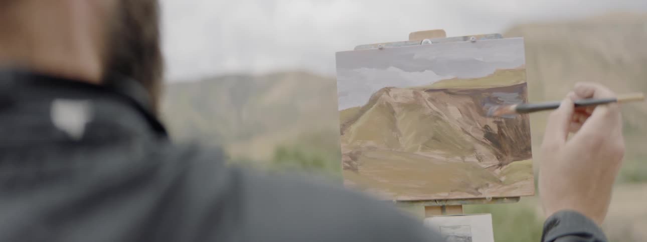 Person painting a picture of hillside with the hillside in the background