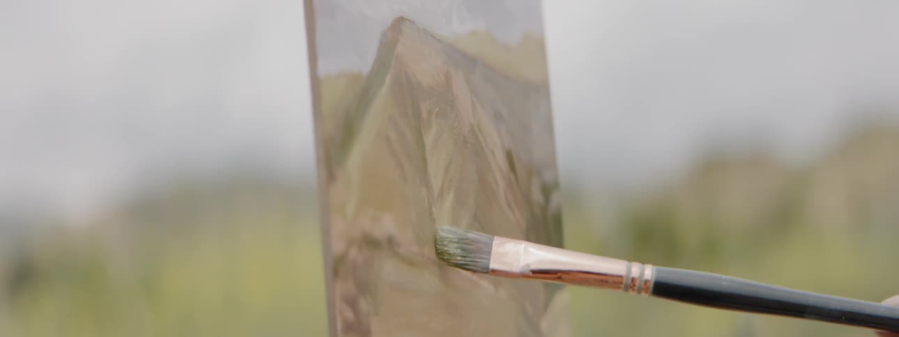 A person paints a mountain landscape on a small canvas