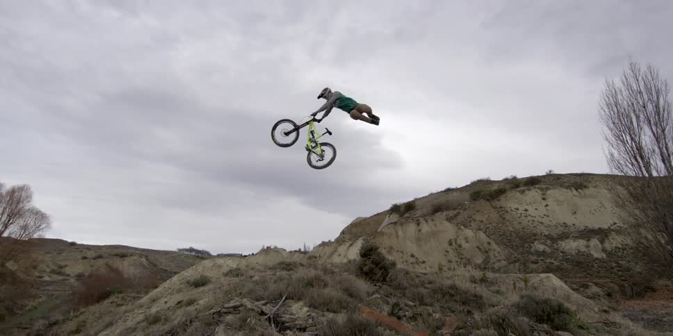 A bmx rider approaches a jump and performs an acrobatic trick