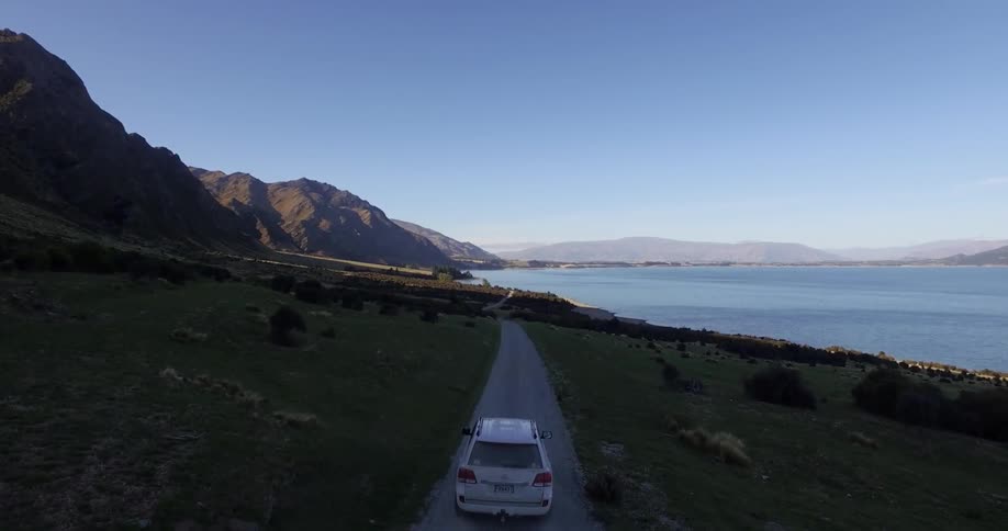 Car drives towards a lake beside mountains