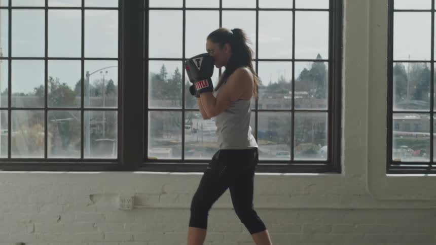 A woman practices boxing in a room with large windows