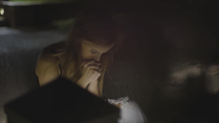 A teenage girl sits in a driveway at night with her hands folded under her face
