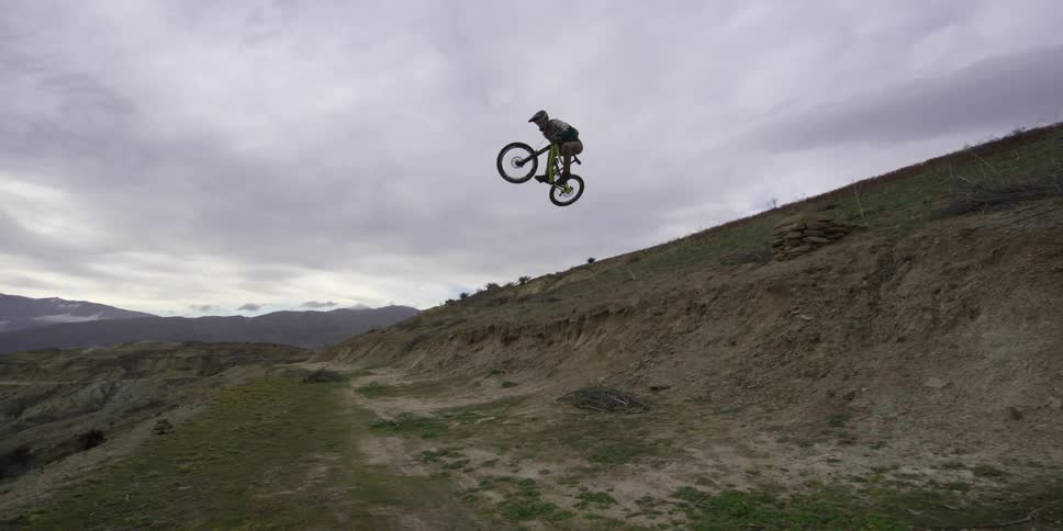 A man rides his bike downhill doing a jump at the end