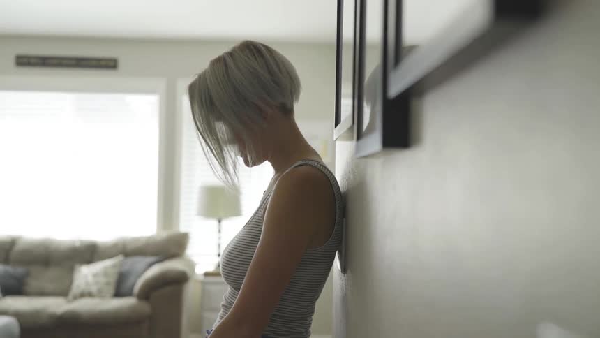 A woman standing against a wall looking down