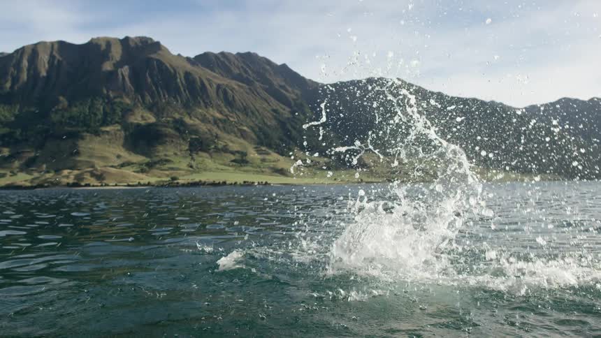 A man dives and swims in a lake back dropped by mountains