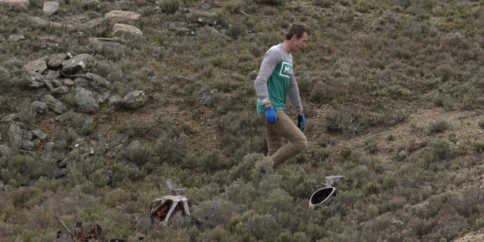 A man walks along a cliffside and throws his bike helmet to the ground