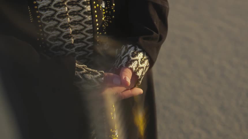 A person standing on sand with a black robe