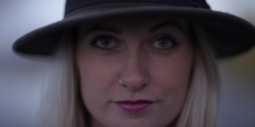 A woman is shown with a hat and piercing