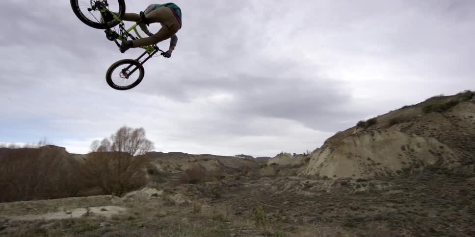 A bicyclist jumps over a dirt hill and flies off the bike