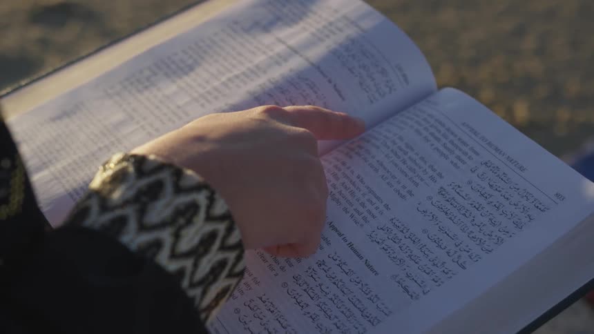 A person uses their finger to read a book outside at sunset