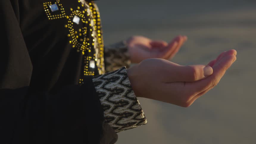 A woman wearing an intricately designed dress prays or meditates