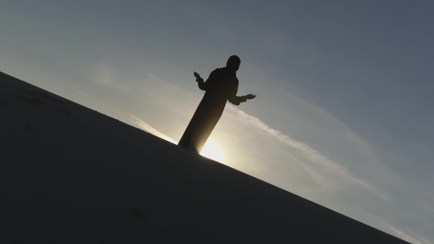 A silhouette of a person with their hands out to their sides standing on a hilltop
