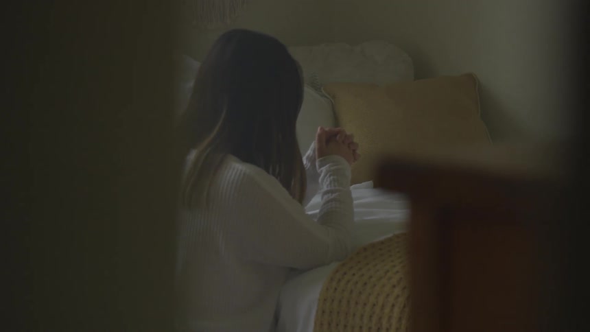 Woman is praying on her knees by her bed