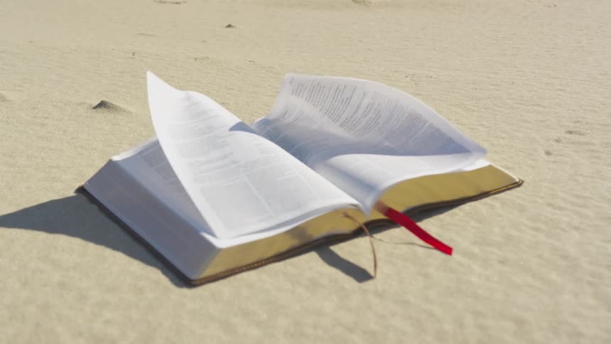 A book sits on sand as the wind blows its pages around
