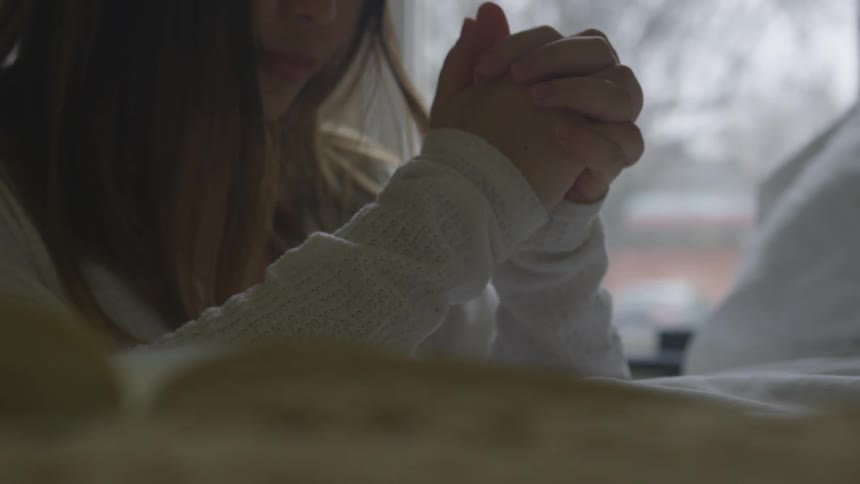 A woman clasps her hands in prayer