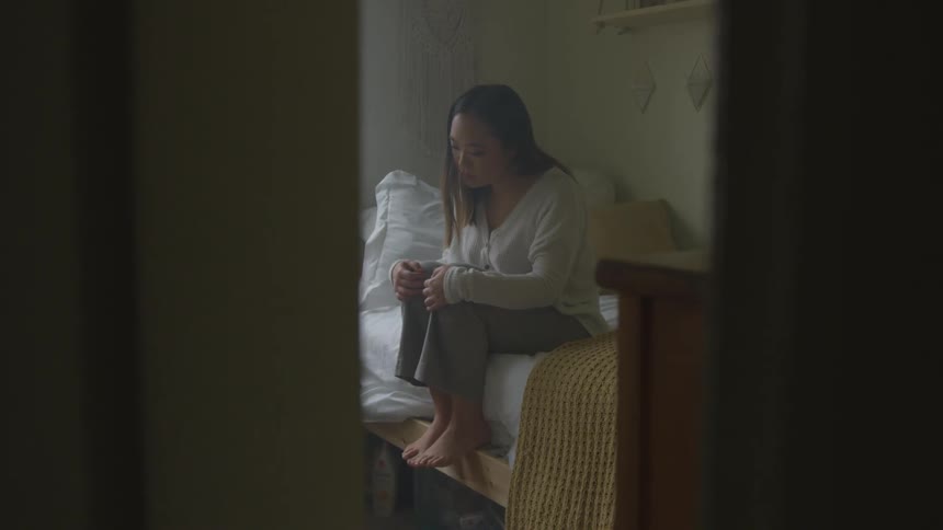 Woman sits on a bed with her hands on her knees