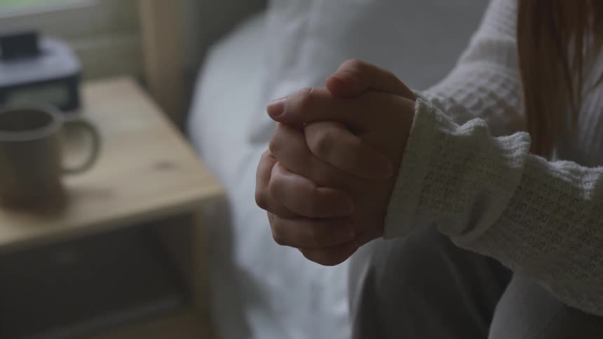 A woman sitting on a bed with her hands clasped