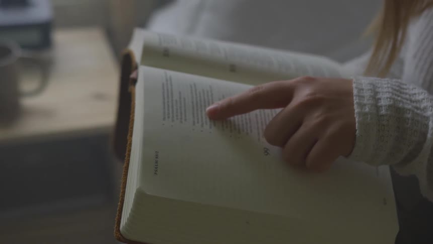 A woman is reading a bible while following along with the text with her finger