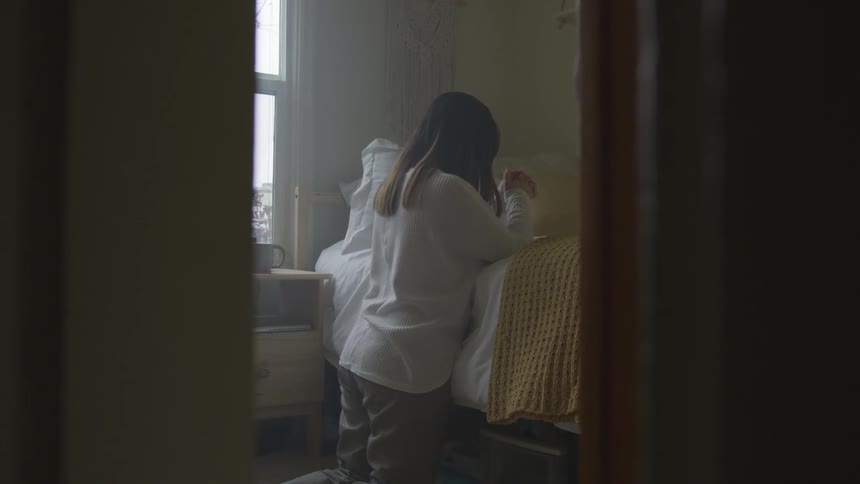 A girl kneels by her bed and prays