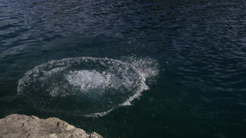 Man jumps off rocks and does a cannonball  into lake