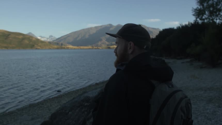 A bearded man carrying a backpack walks towards the shoreline