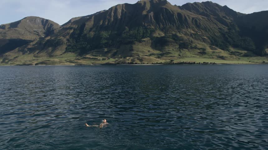 A man swims in a large lake in front of a mountain range