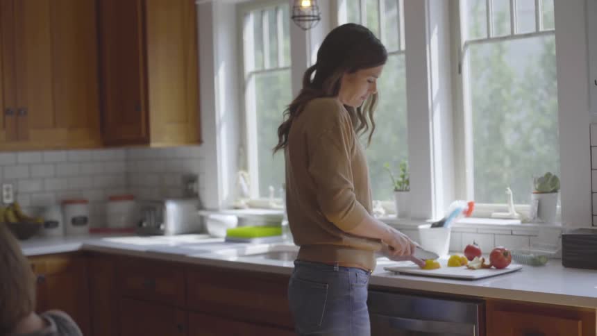 A woman is cutting fruit on a cutting board in a kitchen