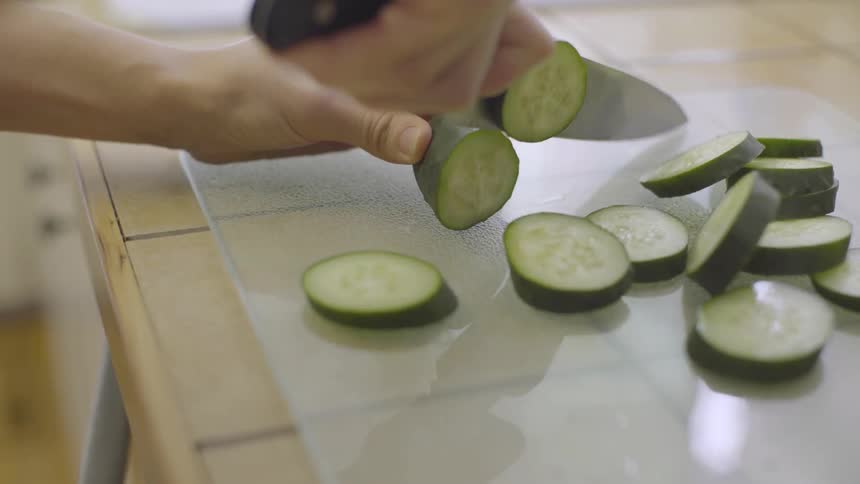 A person chopping cucumbers on a countertop