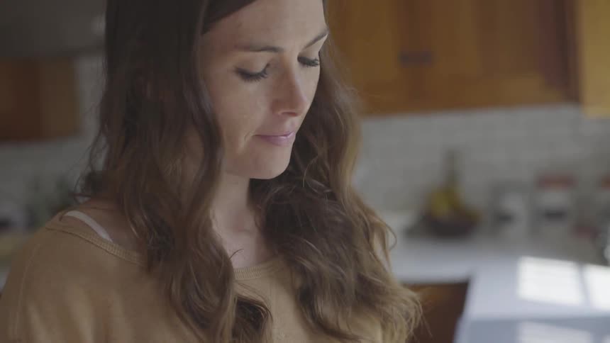 A brunette white woman standing in a kitchen looking downward