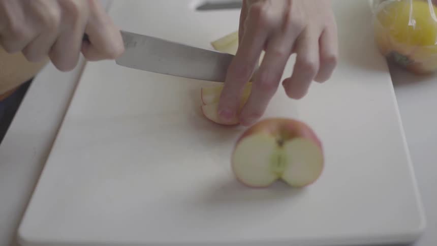 Apples being cut and sliced by someone on a white cutting board
