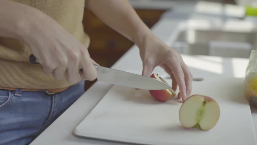 A white woman uses a knife to cut an apple in half
