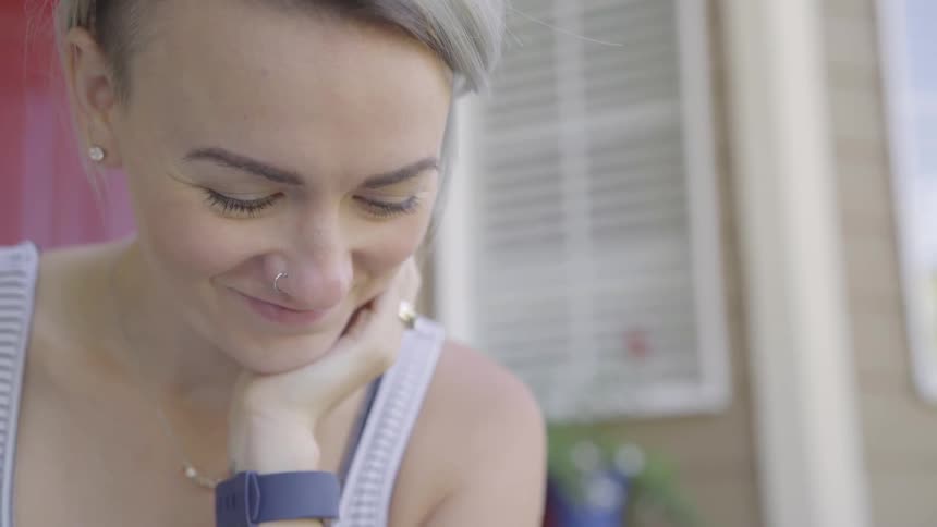 Blonde woman wearing wrist watch touches her hair and smiles in the daytime