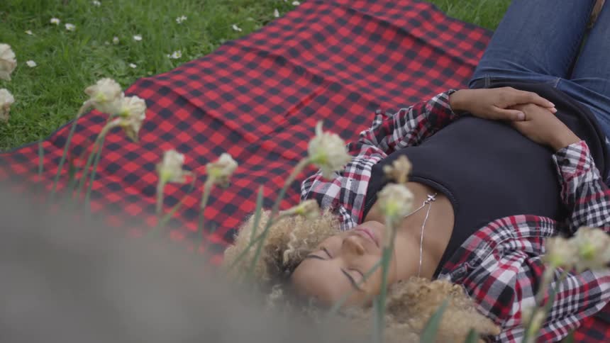 A woman lies on a blanket in the grass with a row of wilting flowers above her head
