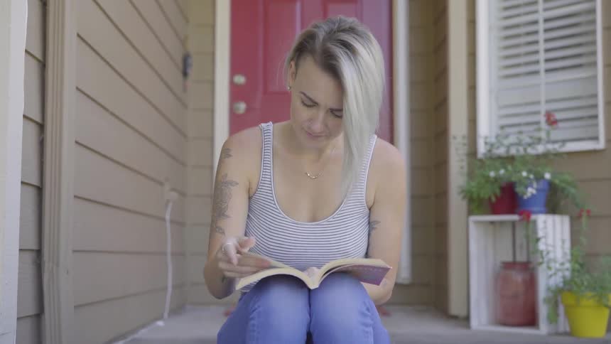 A woman sits on a stoop and reads a book