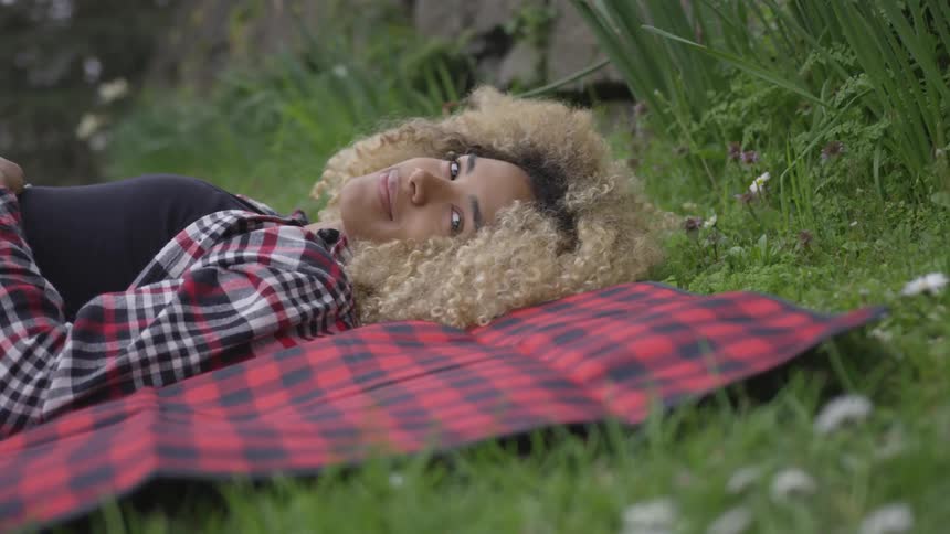 A woman lays on a blanket in the grass