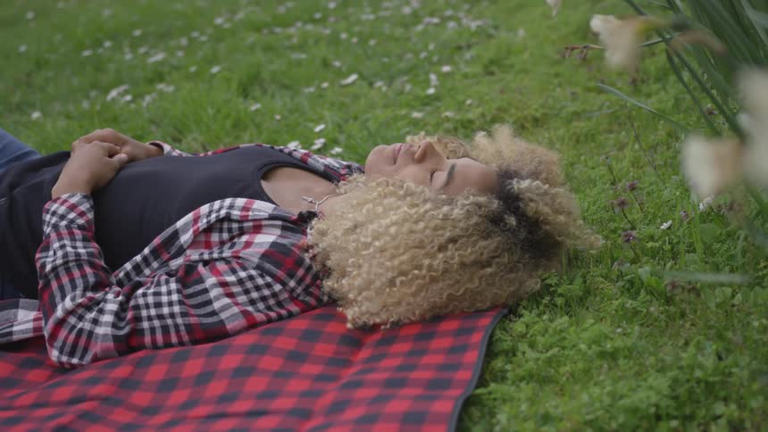 Female with curly hair wearing a flannel laying on a blanket on the grass