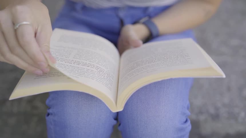 A female sits on a step turning the pages of a book she's skimming through