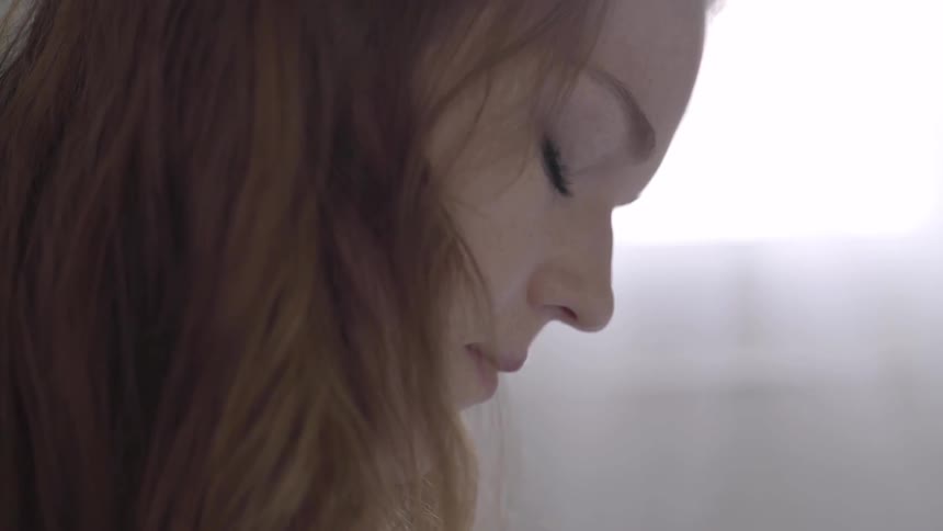 A young woman with brown hair looks downward as she concentrates on something that she's doing